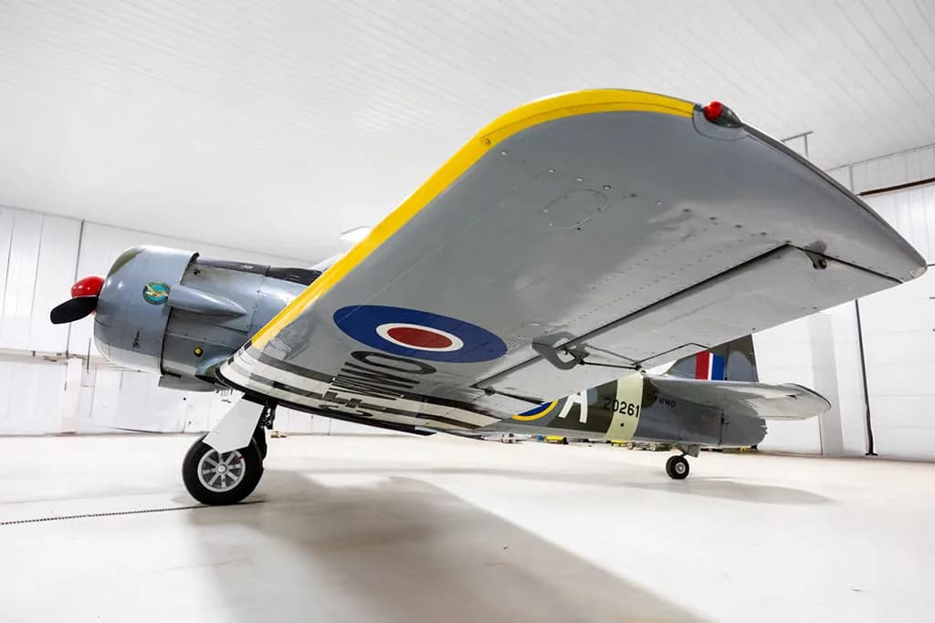 A low-angle view of a North American Harvard Mk.IIB aircraft, showing the underside of its wing with a yellow leading edge and RAF roundel.