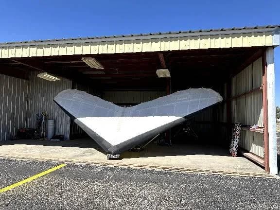 A white and black delta-wing aircraft is stored inside an open hangar.