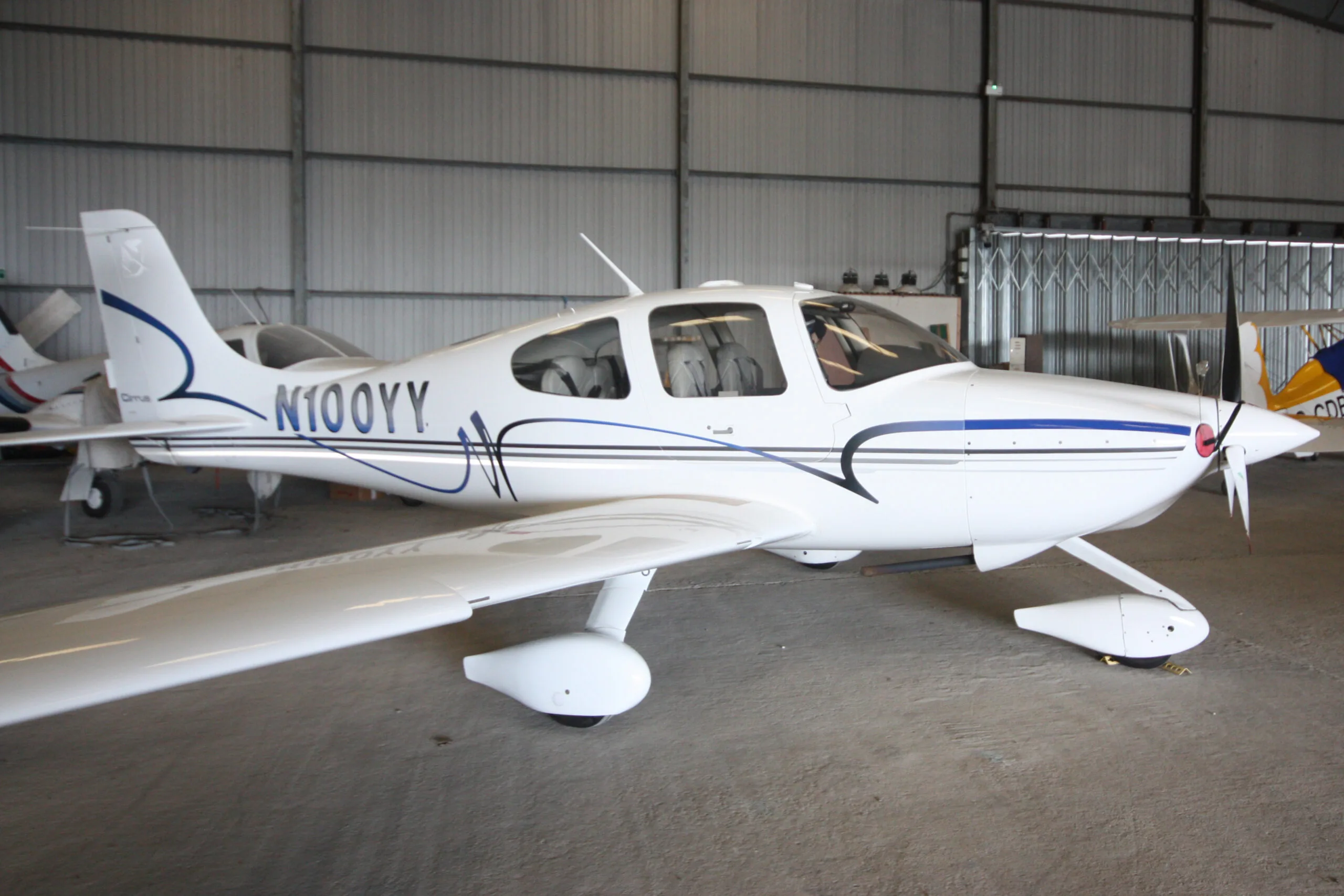 A white Cirrus SR22 aircraft with blue and grey stripes parked inside a hangar.