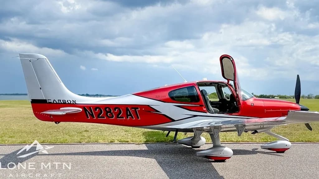 A red and silver Cirrus SR22T aircraft, registration N282AT, with its doors open, parked on an airfield under a cloudy sky.