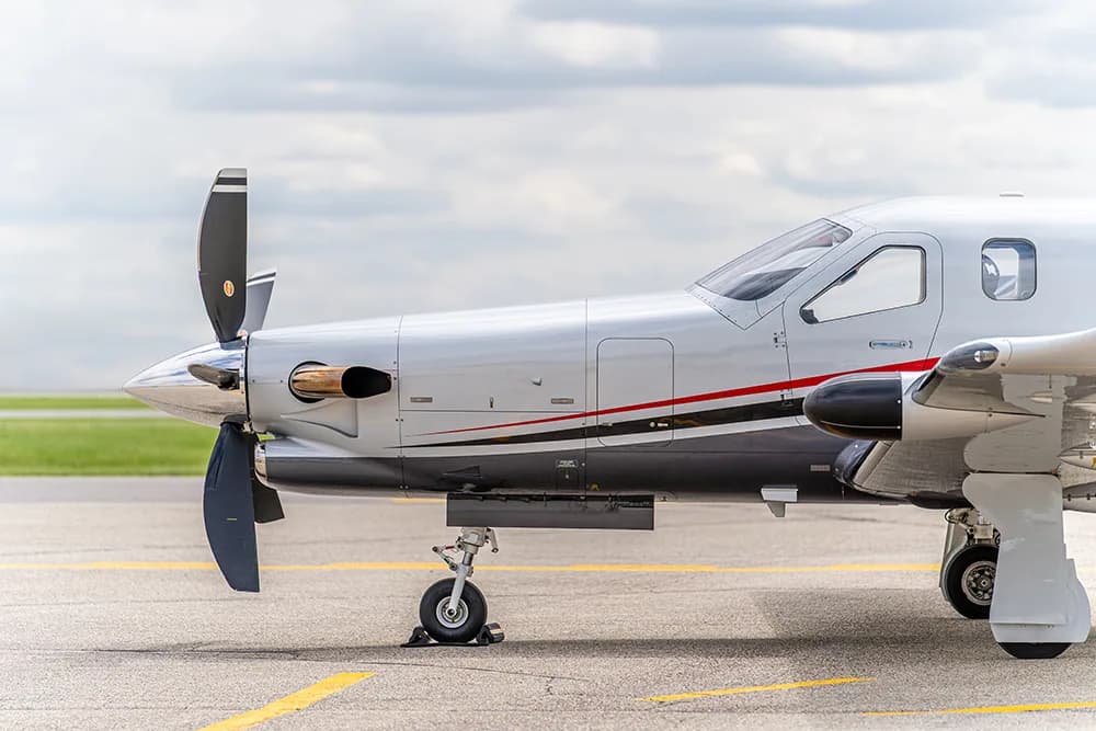 A close-up side view of the nose and propeller of a silver and black TBM turboprop aircraft on the tarmac.