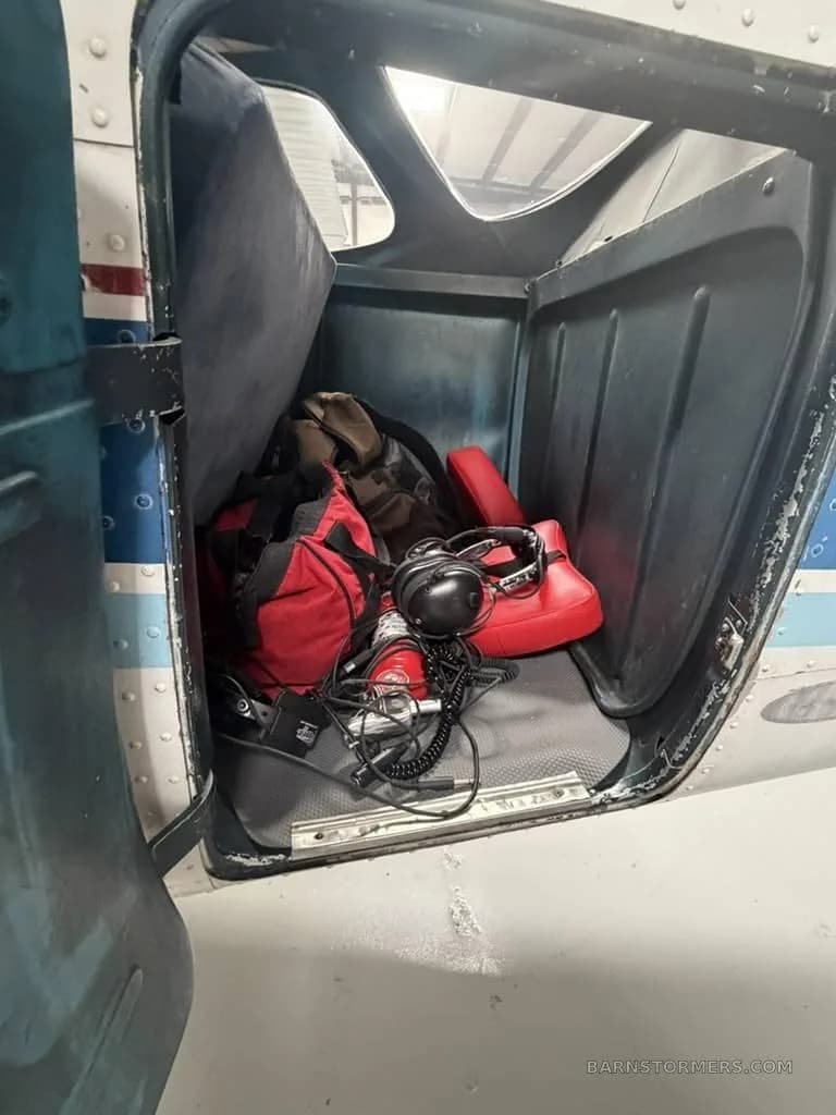 The baggage compartment of a Cessna 172, filled with a red bag, headsets, and other gear.