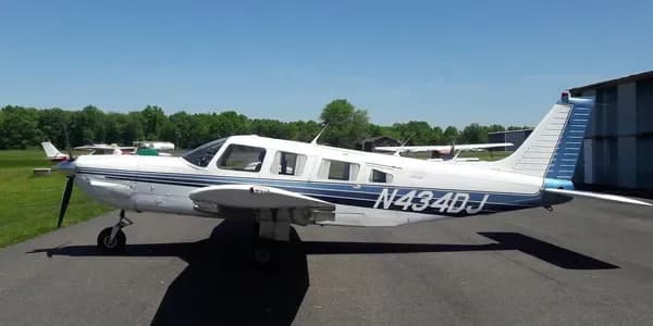 A white Piper PA-32R-300 Cherokee Lance with blue stripes, registration N434DJ, parked on an airfield tarmac.