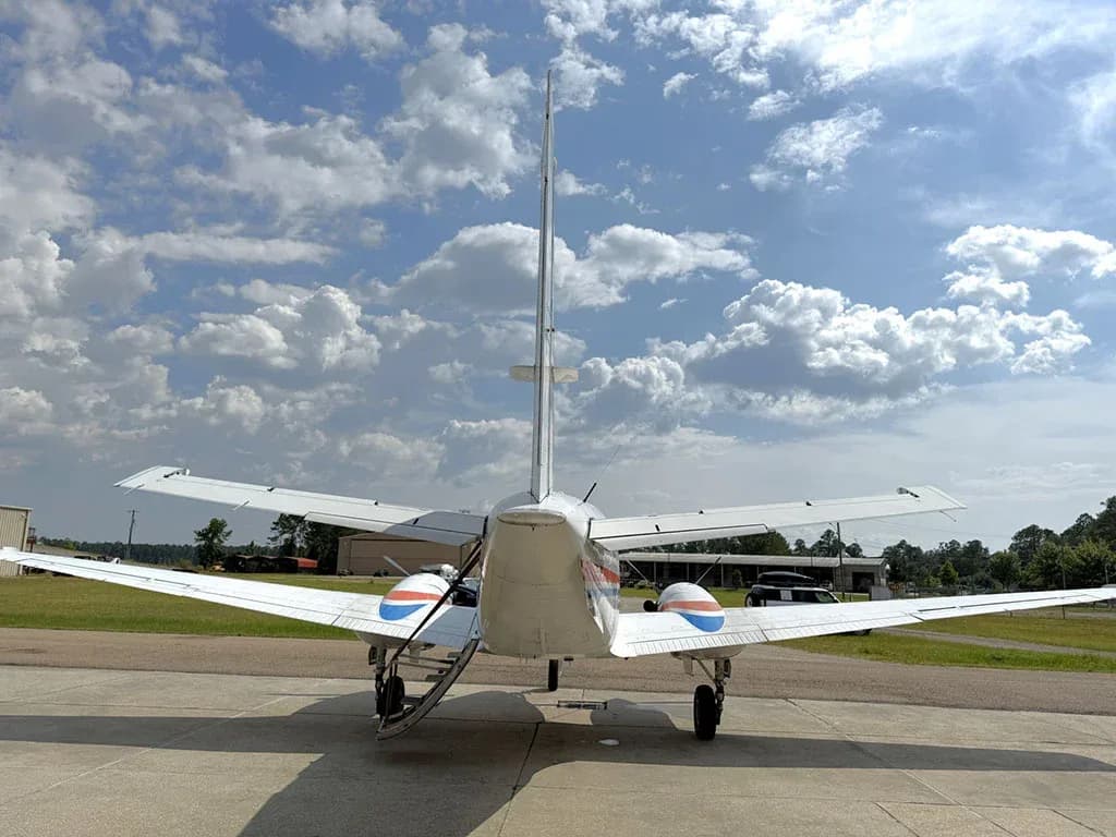 A rear view of a white twin-engine turboprop aircraft with blue and orange accents on the engine nacelles, parked on a tarmac.