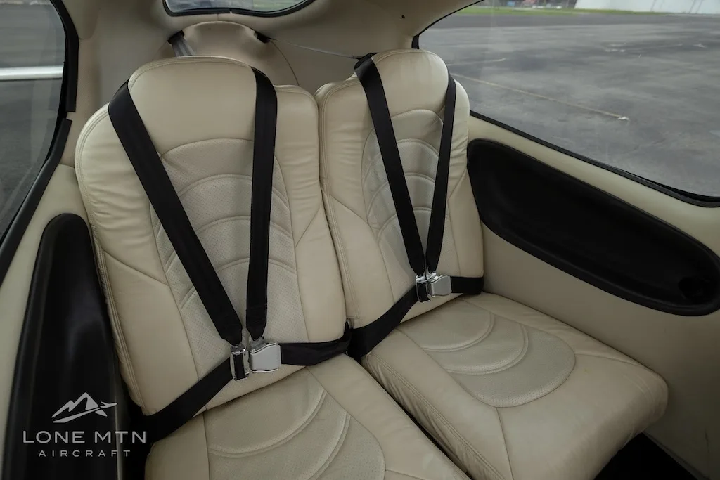 A side view of two beige leather rear seats with black seatbelts in the aircraft cabin.