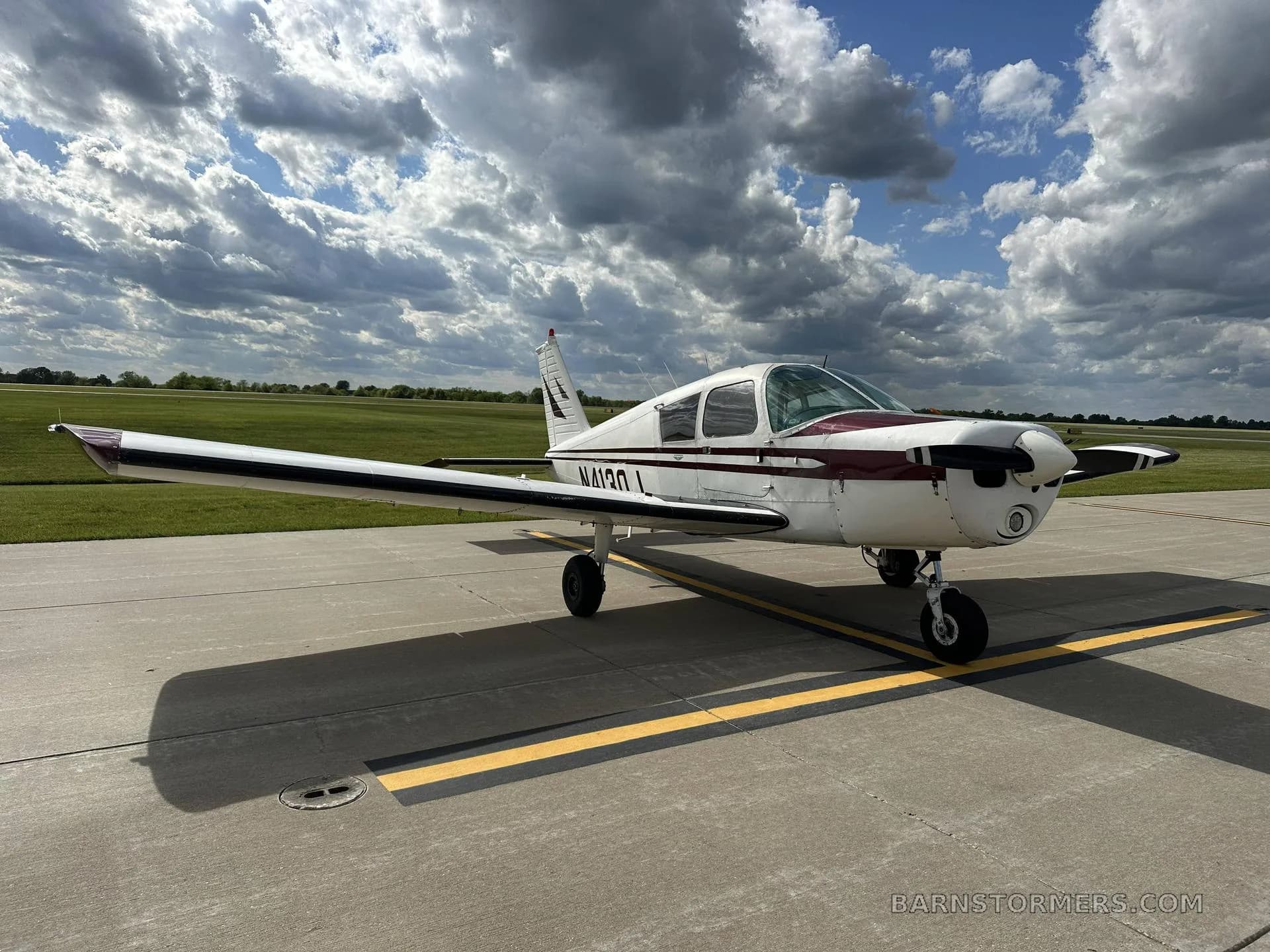 A white and maroon single-engine propeller aircraft, registration N4120J, is parked on an asphalt ramp under a partly cloudy sky, viewed from the front-right.