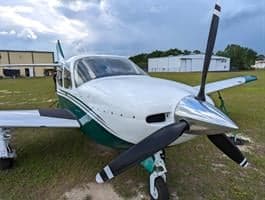 A white and green Commander 114B aircraft is parked on the grass.