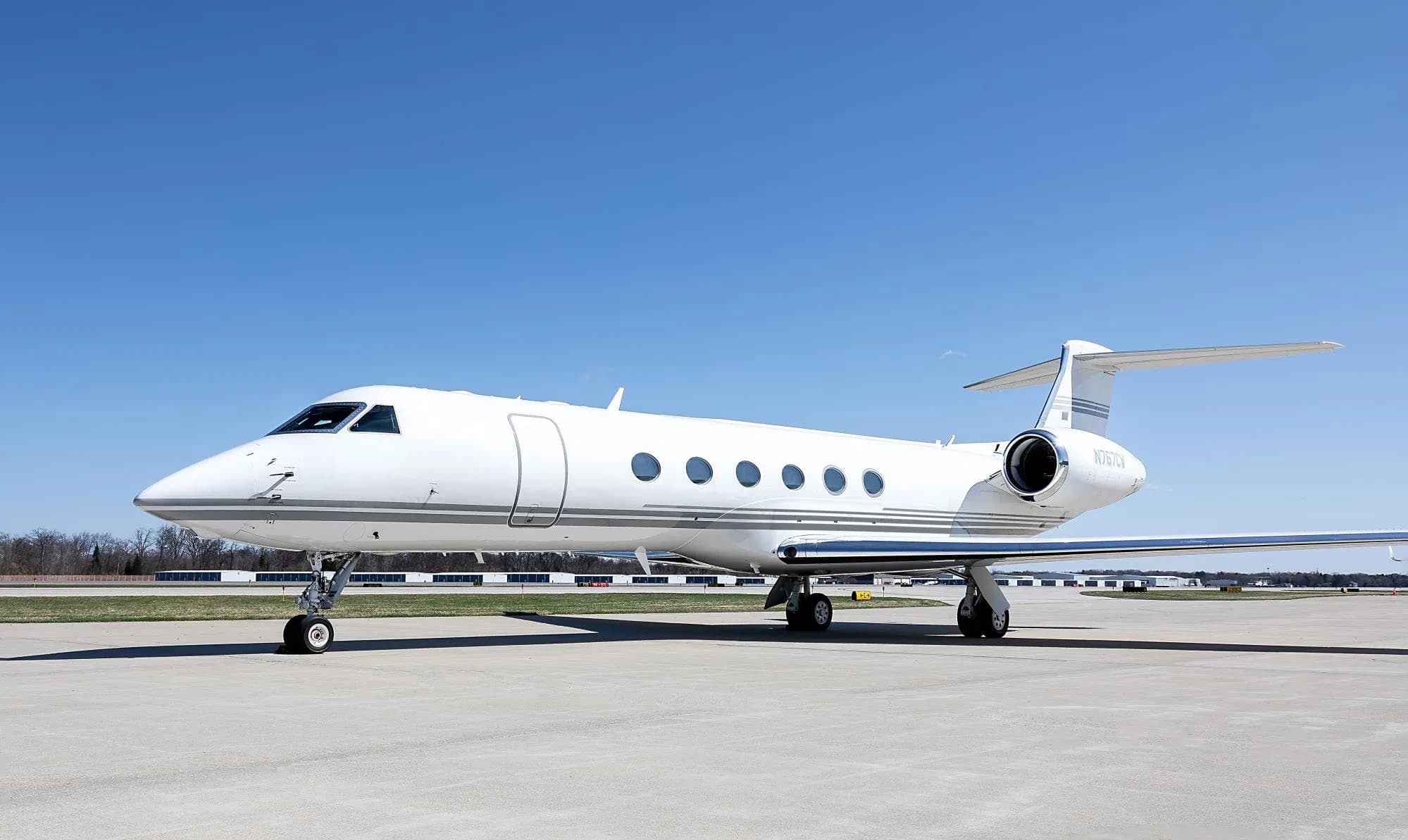 A white Gulfstream G550 business jet with registration N767CW parked on an airfield under a clear blue sky.