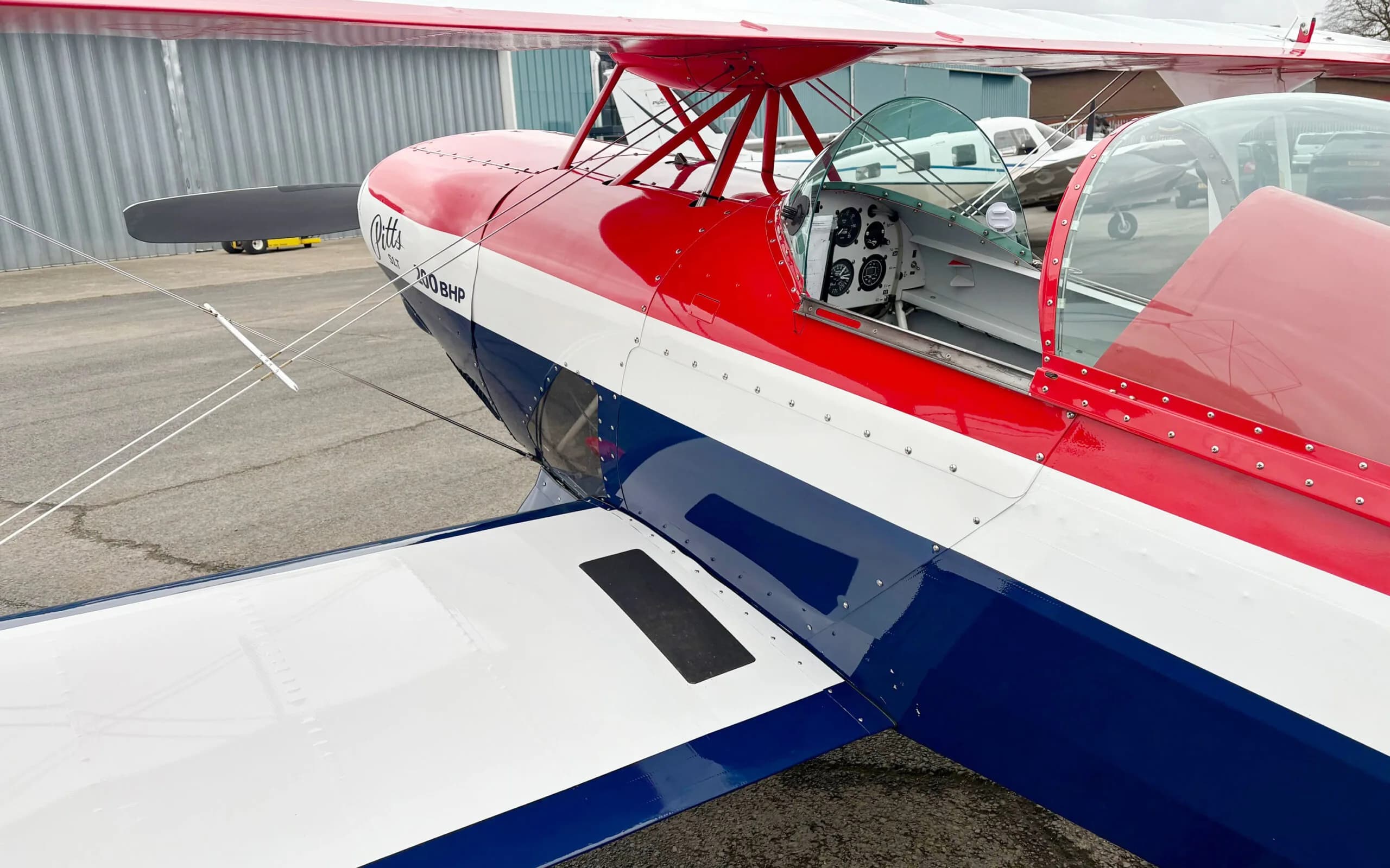 A side view of the red, white, and blue Pitts S1T biplane, showing the open cockpit and upper wing.