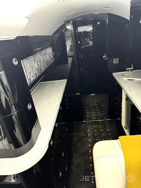 A detailed view of the private jet's galley area with sleek black cabinetry, light countertops, and a patterned floor.