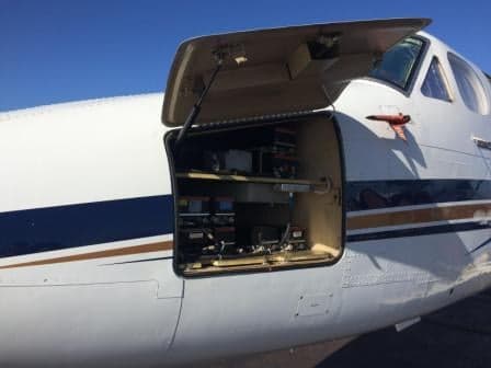 An open panel on the side of a King Air aircraft reveals internal equipment.