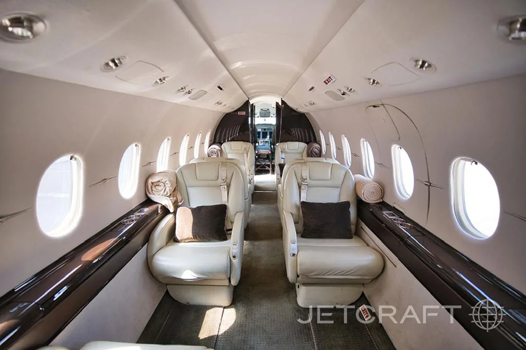 The aircraft's cabin features light-colored leather seats with dark pillows and rolled blankets.