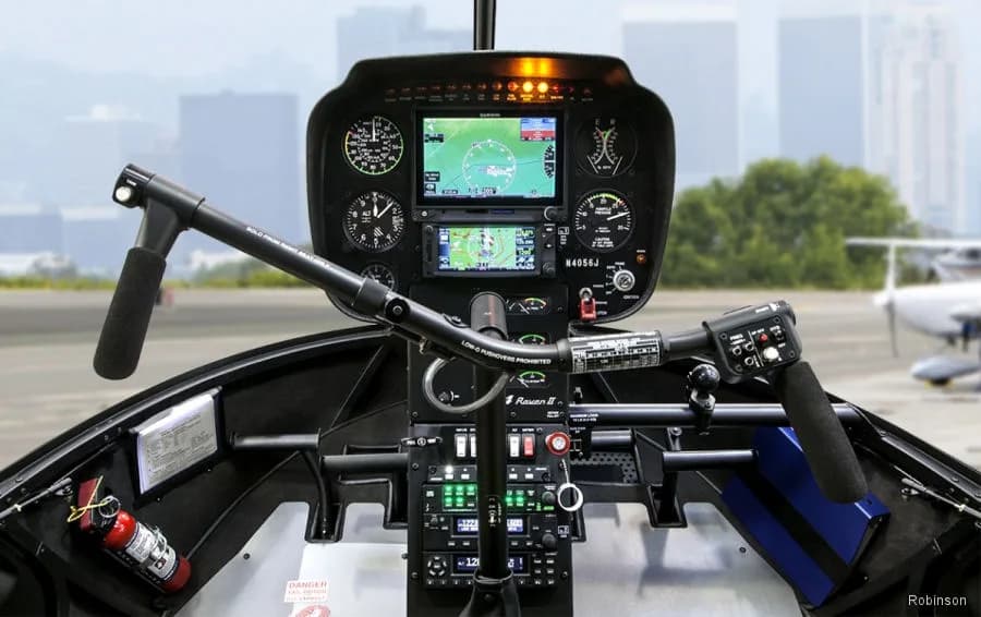 The cockpit of a Robinson R44 helicopter showing the instrument panel, cyclic, and collective controls.