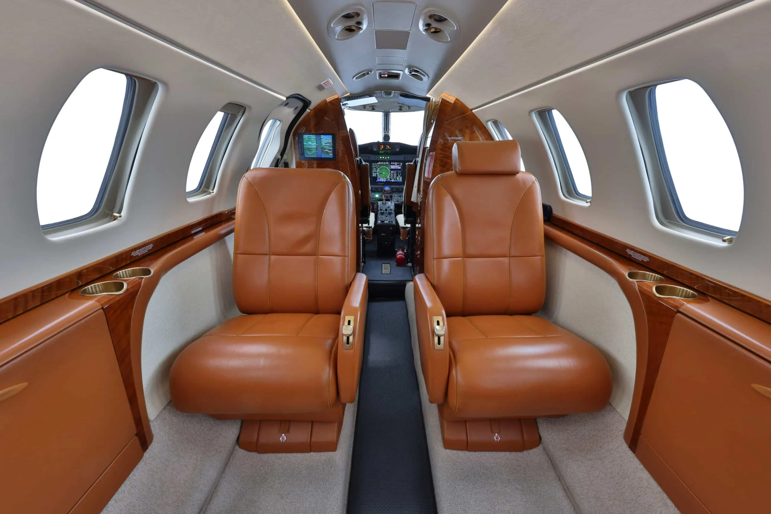 View of a private jet cabin with tan leather seats looking towards the cockpit.