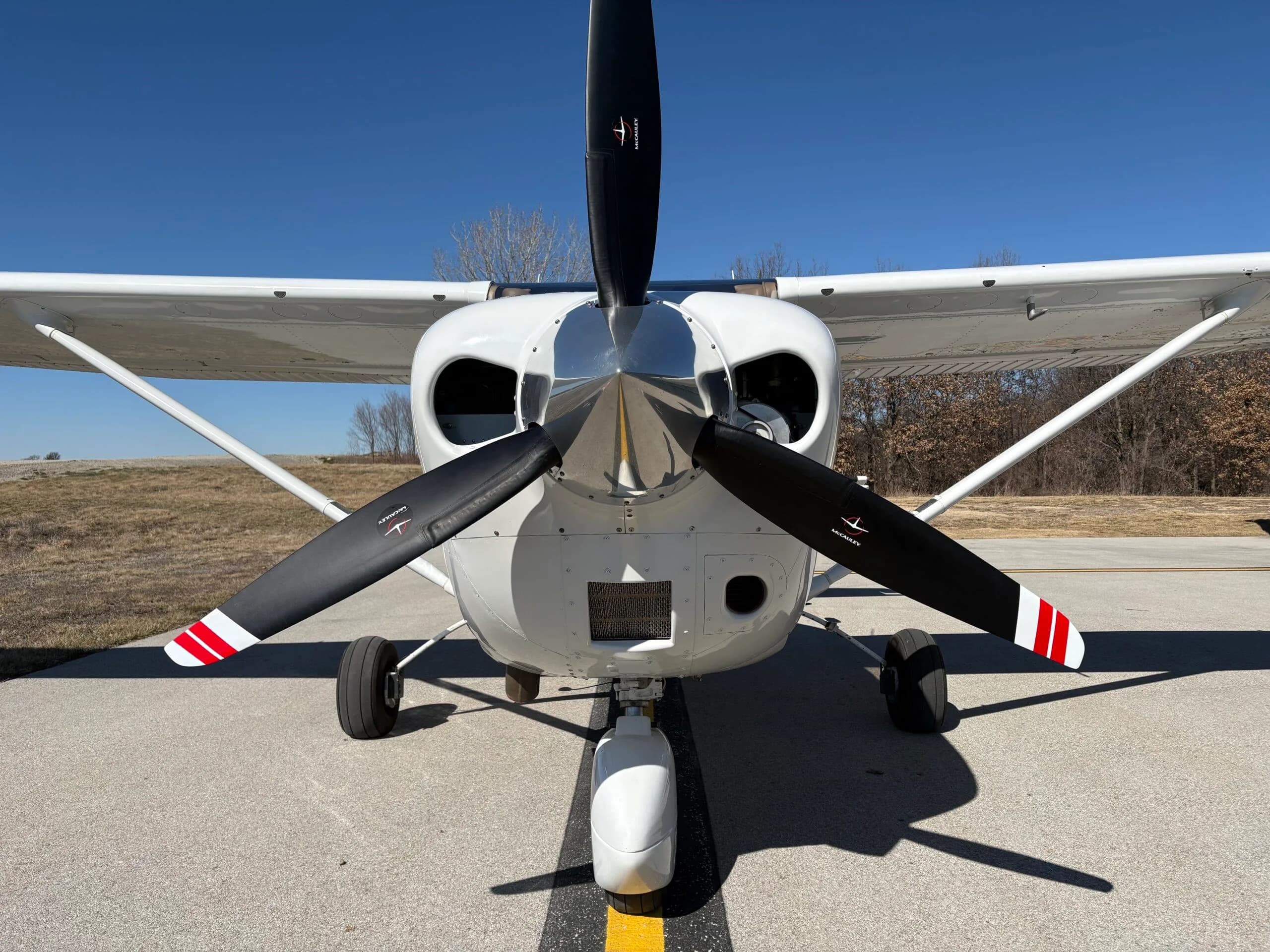 Close-up front view of the propeller and nose of a white single-engine aircraft.