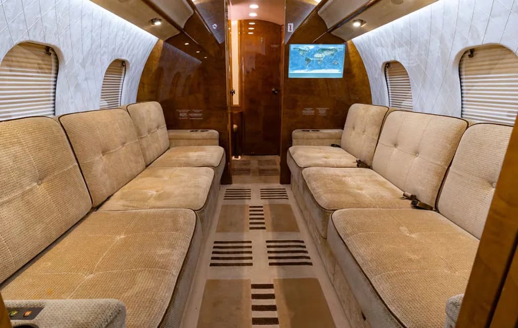 The aft section of a private jet cabin featuring two long, comfortable beige sofas facing each other.