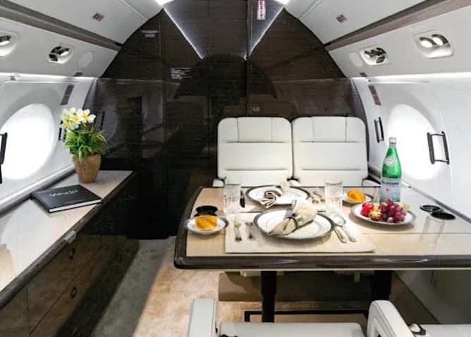 View of the aircraft cabin with white leather seats and a dining table.