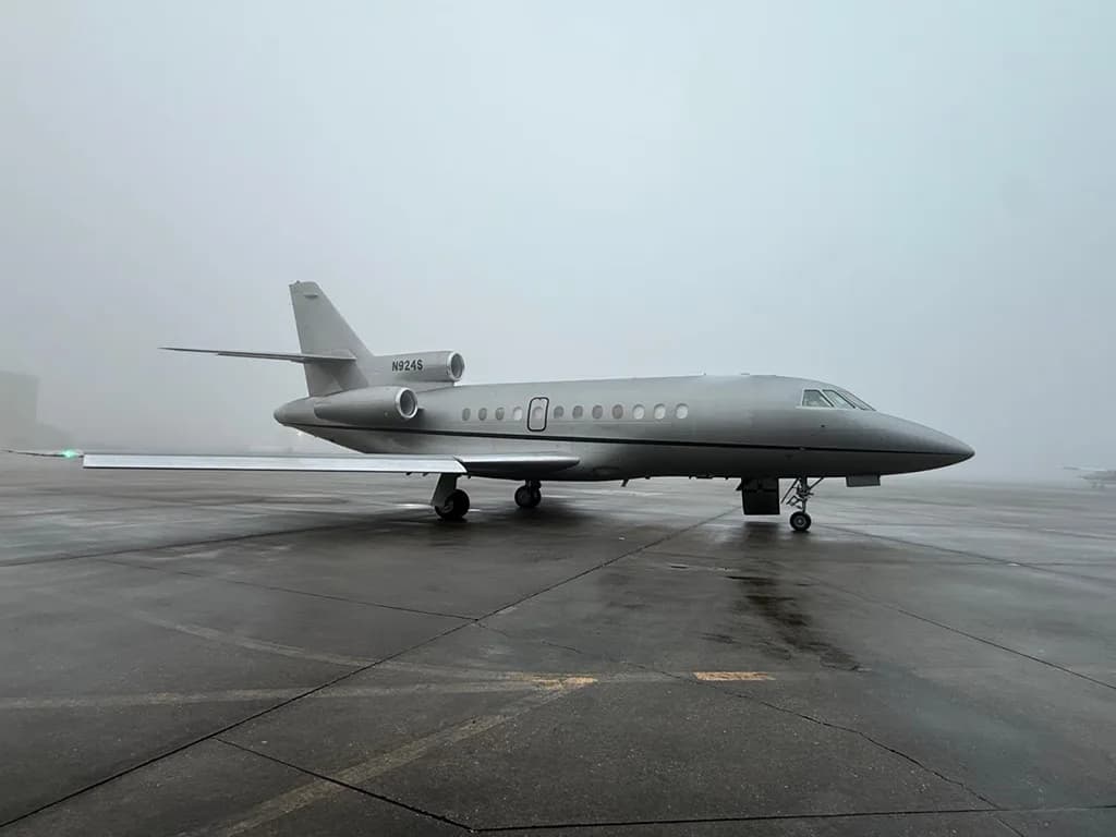 A Dassault Falcon 900EX business jet, registration N924S, in a grey paint scheme, parked on a wet tarmac in foggy weather.