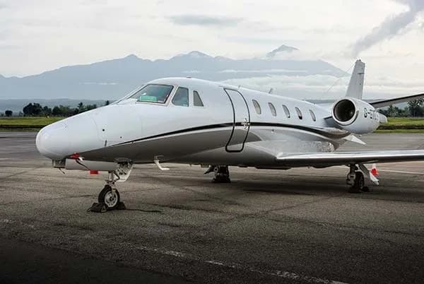 Front side view of the G-GXLS Cessna Citation on the tarmac with mountains in the background.