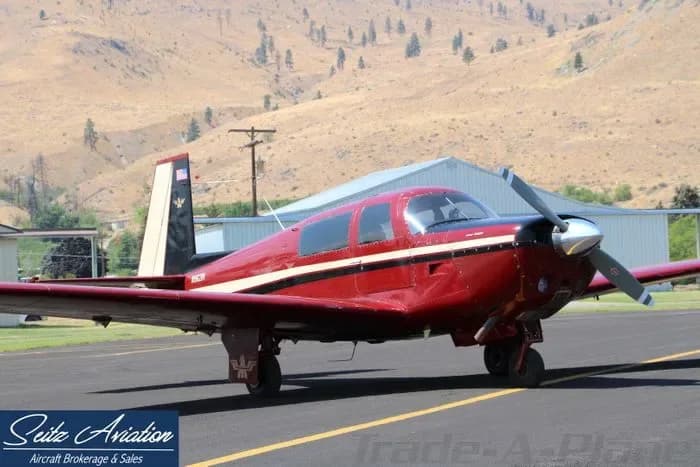 A red and white Beechcraft Bonanza parked on the tarmac in front of a hangar.