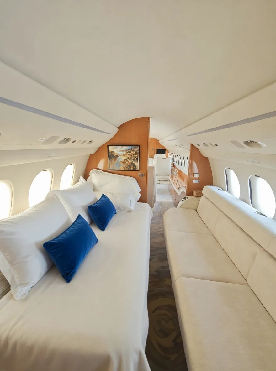A view of the aft aircraft cabin showing a bed with white linens and blue pillows, and a long white sofa.