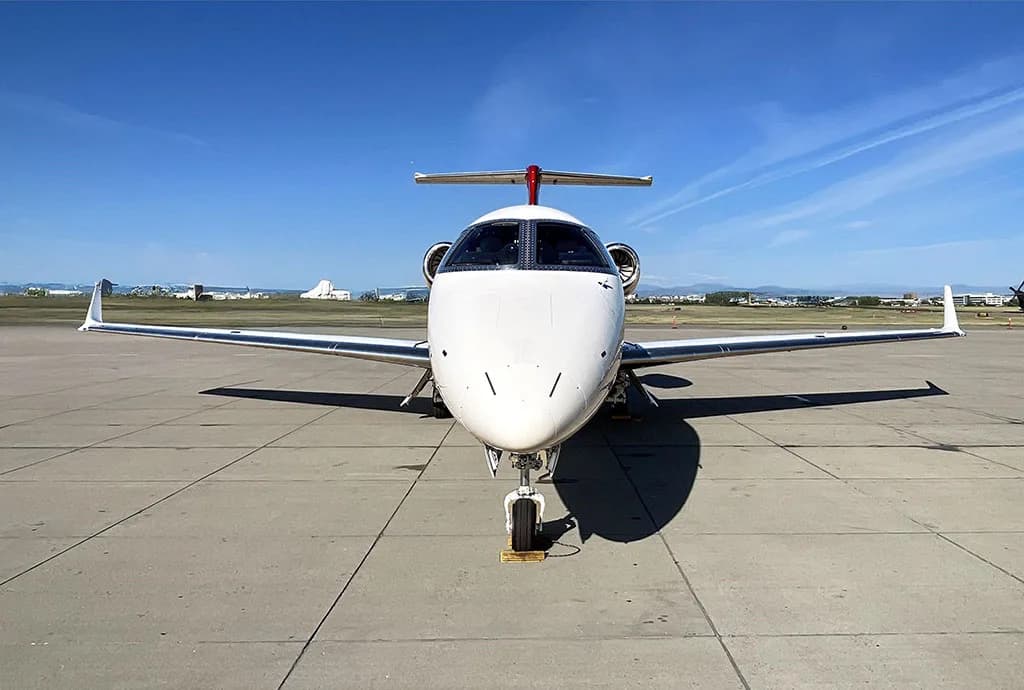 A head-on view of a white and red Embraer Phenom 300 private jet parked on an airport tarmac.