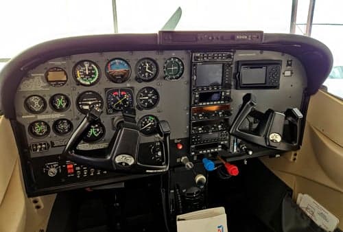 The cockpit of a Cessna 182 Skylane, showing the instrument panel with analog gauges and modern avionics.