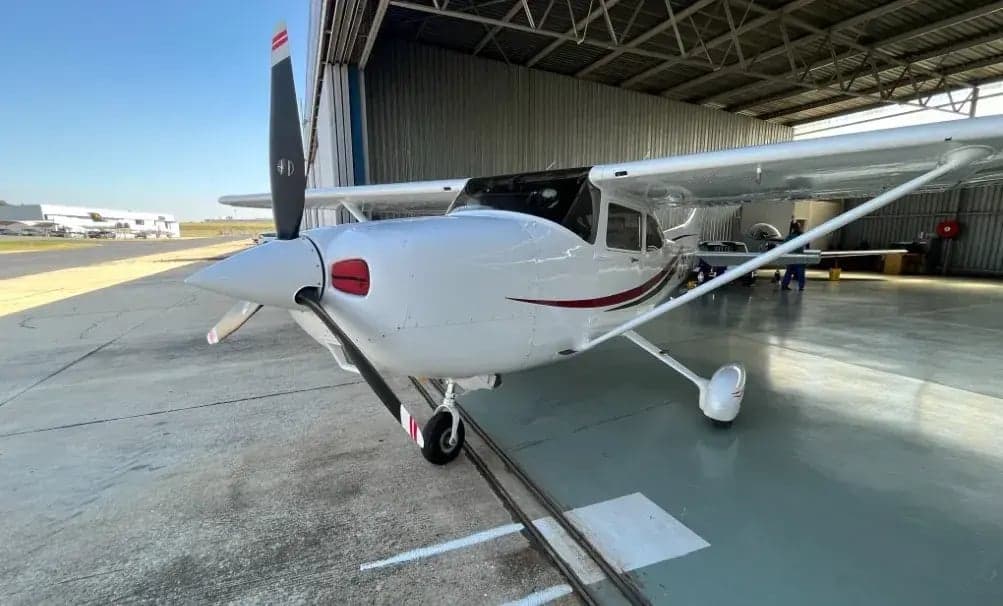 Close-up of a Cessna aircraft parked inside a hangar, highlighting its white paint scheme with red and blue accents.