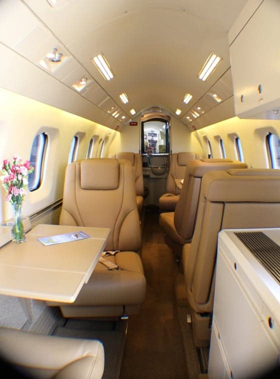 View of the aircraft cabin with tan leather seats and a table with flowers.