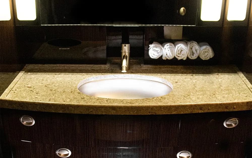 An aircraft lavatory with a modern sink, granite countertop, and rolled white towels.
