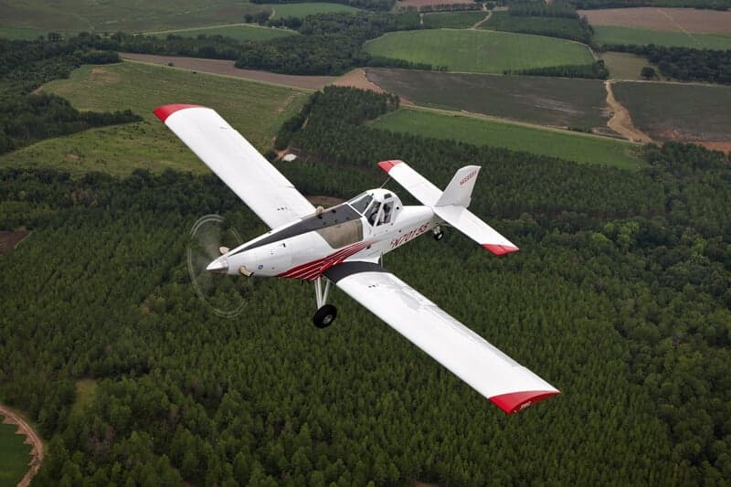 A Thrush aircraft in flight over a rural landscape.