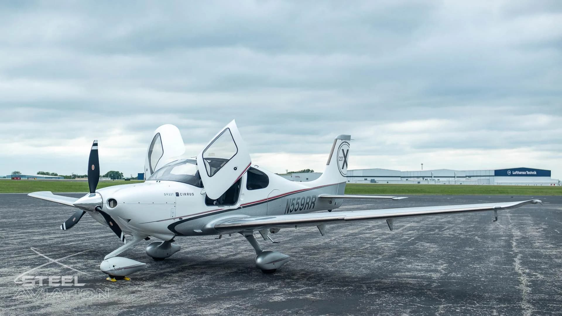A white and silver Cirrus SR22T aircraft with registration N559RR has its gull-wing doors open on an airfield.