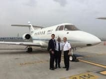 Three people stand in front of a white aircraft on the tarmac.