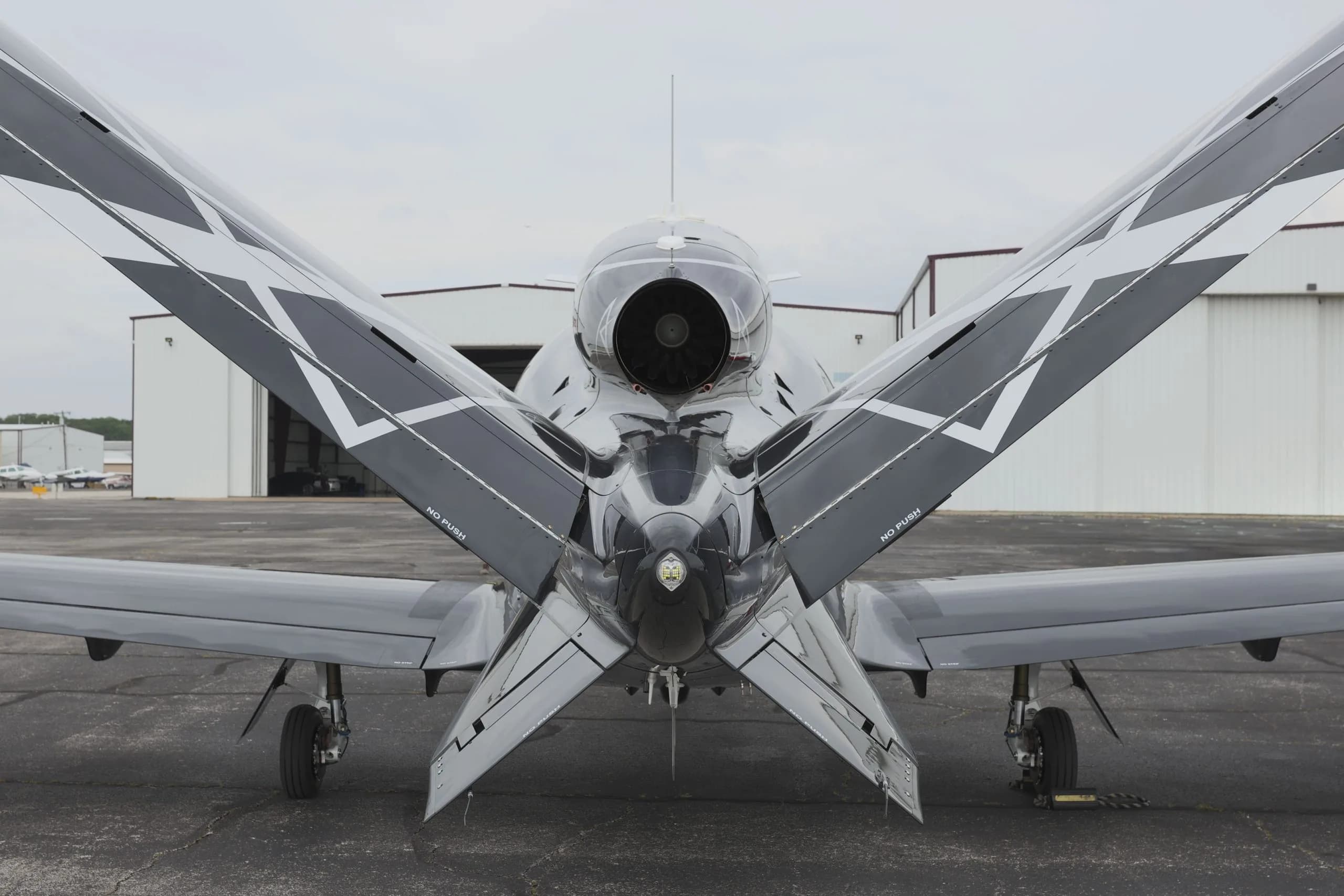 A rear view of a black Cirrus Vision Jet (N25KQ) showing its engine and V-tail with geometric patterns, parked in front of hangars.
