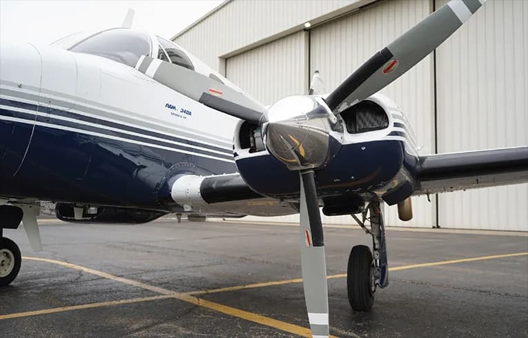 Close up of the propeller and nose of a white and blue Piper PA-34 Seneca aircraft.