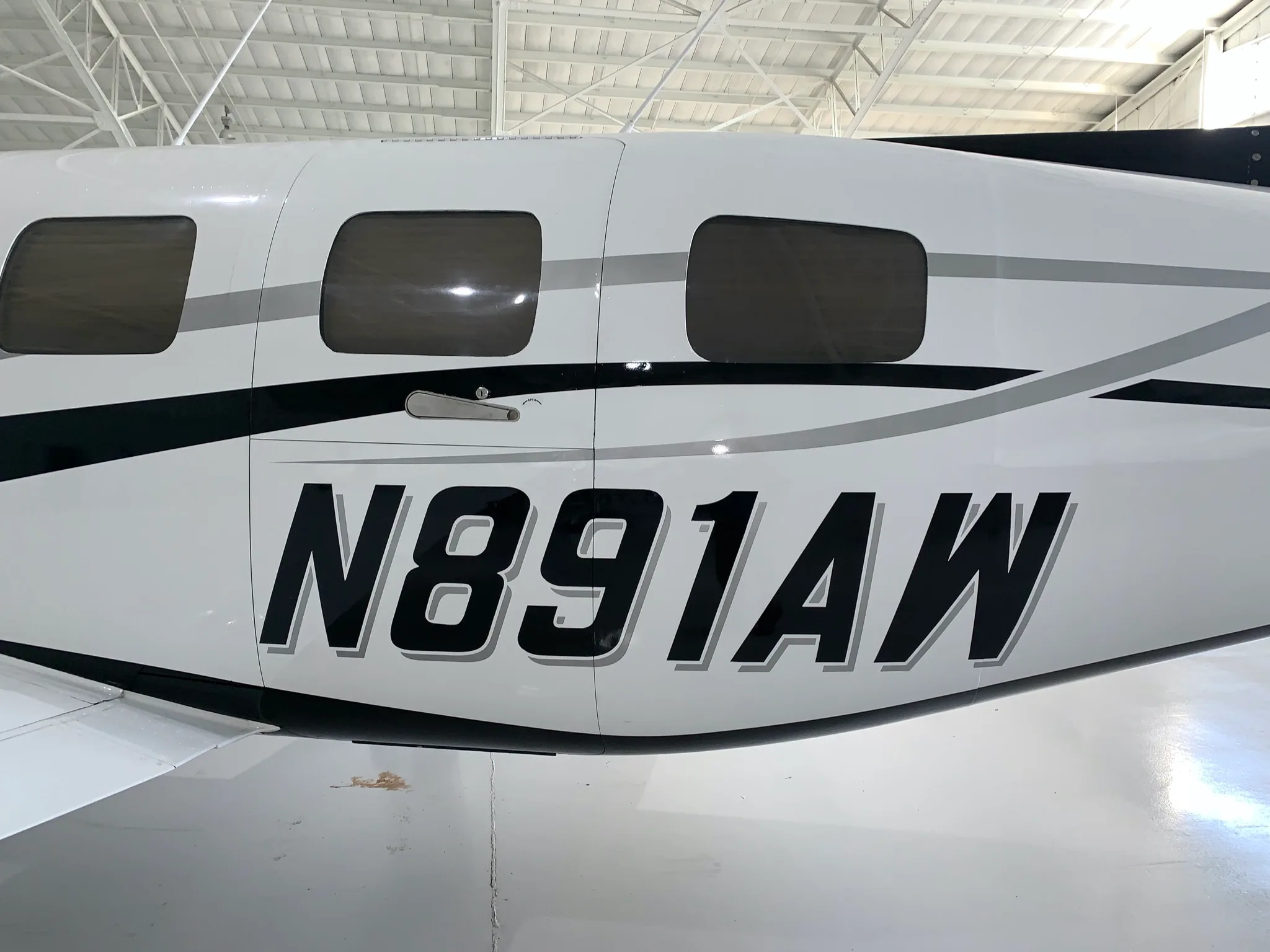 A close-up of the white fuselage of the Piper Mirage aircraft, showing the black registration number N891AW and gray stripe details.