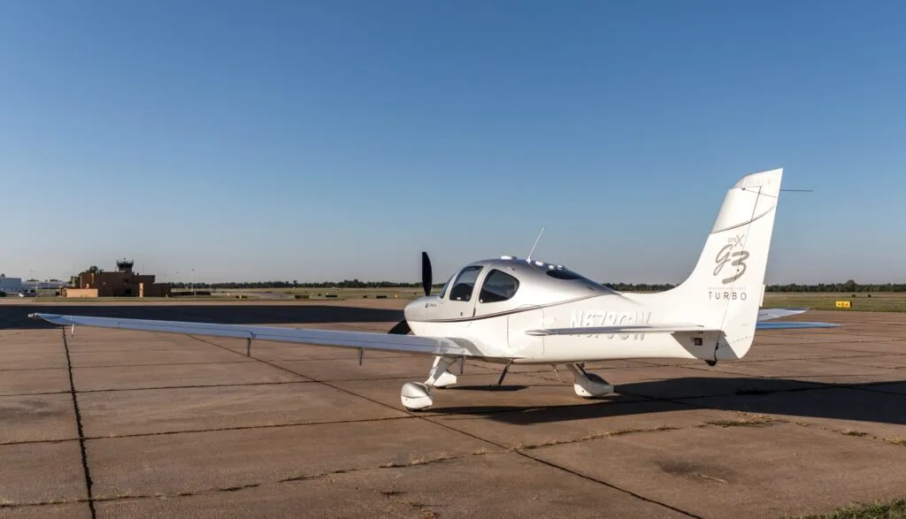 A rear quarter view of a silver and white Cirrus SR22 G3 Turbo aircraft (N678GW) parked on an airfield.