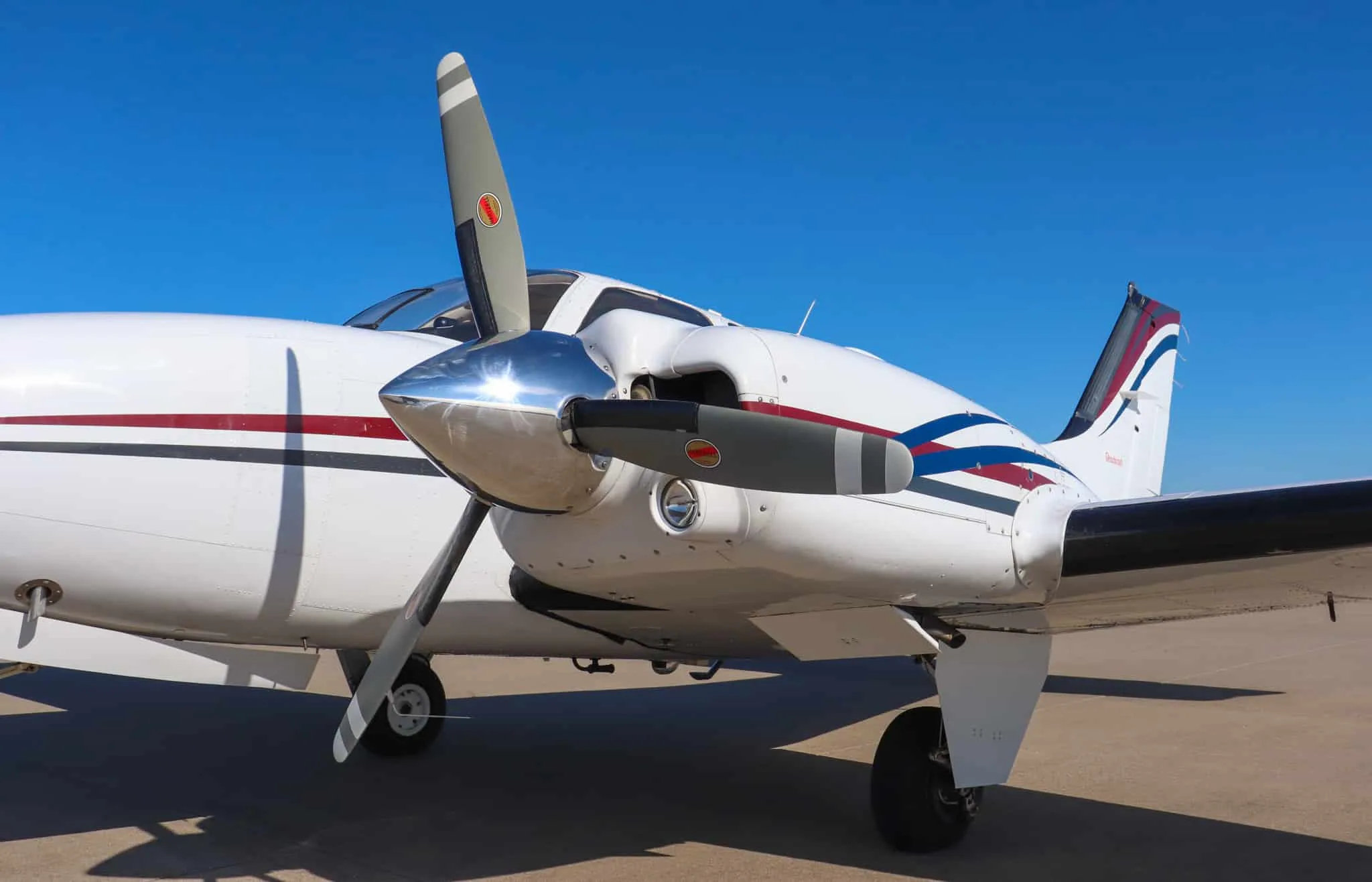 Close-up of the right engine and rear fuselage of a white Beechcraft Baron N204G, showing the red, blue, and gray stripes.