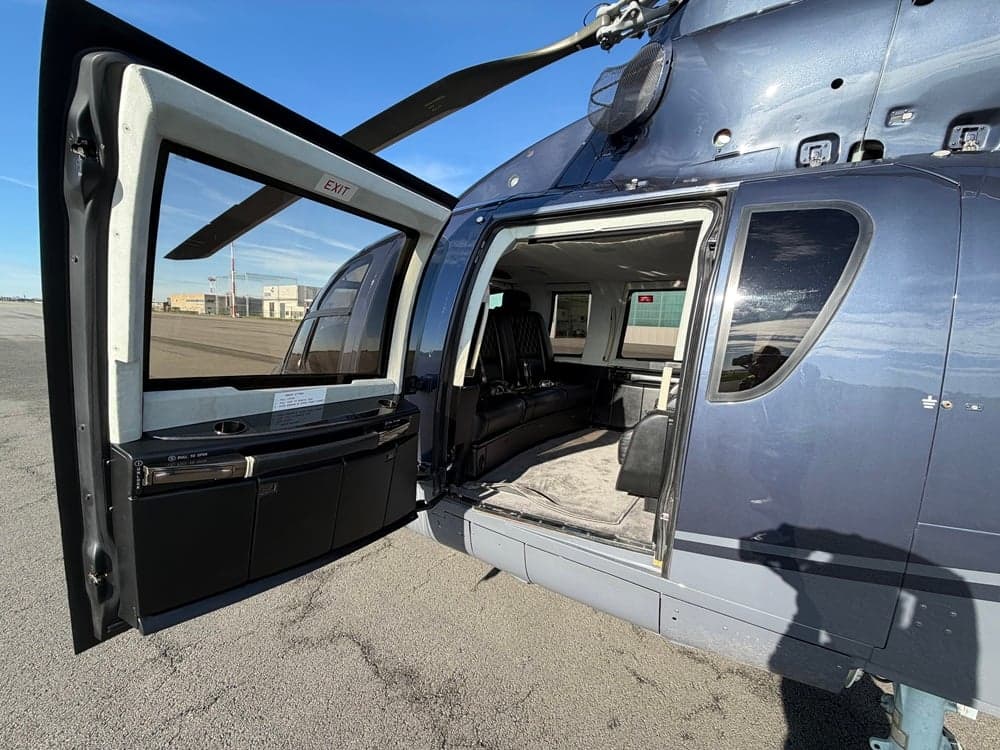The open door of a dark blue helicopter reveals a luxurious black leather interior with a bench seat.