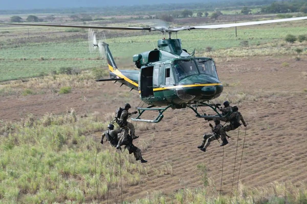 Bell UH-1 Iroquois helicopter with people rappelling from it over a field.