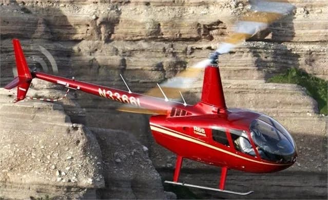 A red Robinson R66 helicopter flying near a canyon.
