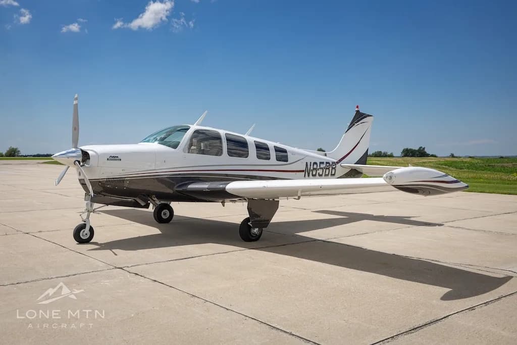 A white and dark grey Beechcraft Baron N85BB parked on a tarmac under a clear blue sky.