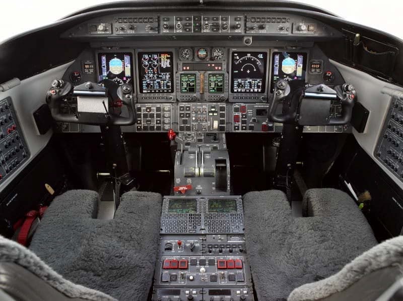 A wide view of the aircraft cockpit, featuring multiple display screens, control yokes, and the center console.