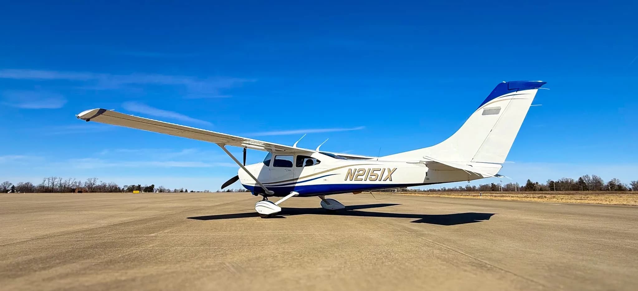 A white and blue Cessna 182 Skylane (N2151X) parked on a tarmac, viewed from the rear-right side.