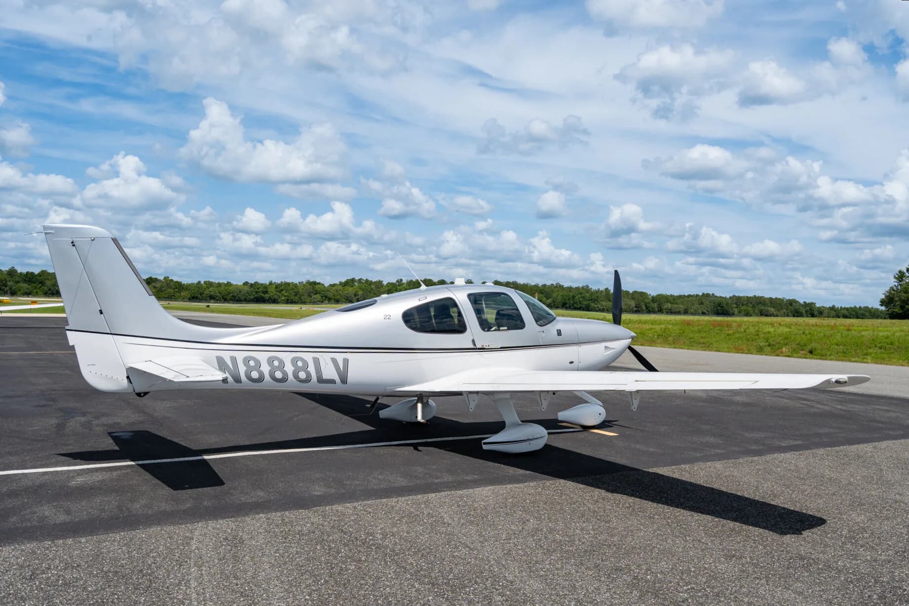 Side view of a silver Cirrus SR22 aircraft (N888LV) parked on an airfield with a clear sky.