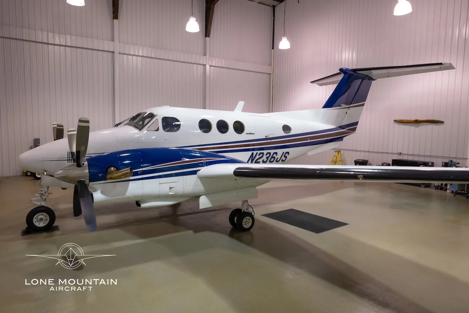 A white and blue twin-engine turboprop aircraft, N236JS, is parked in a hangar.