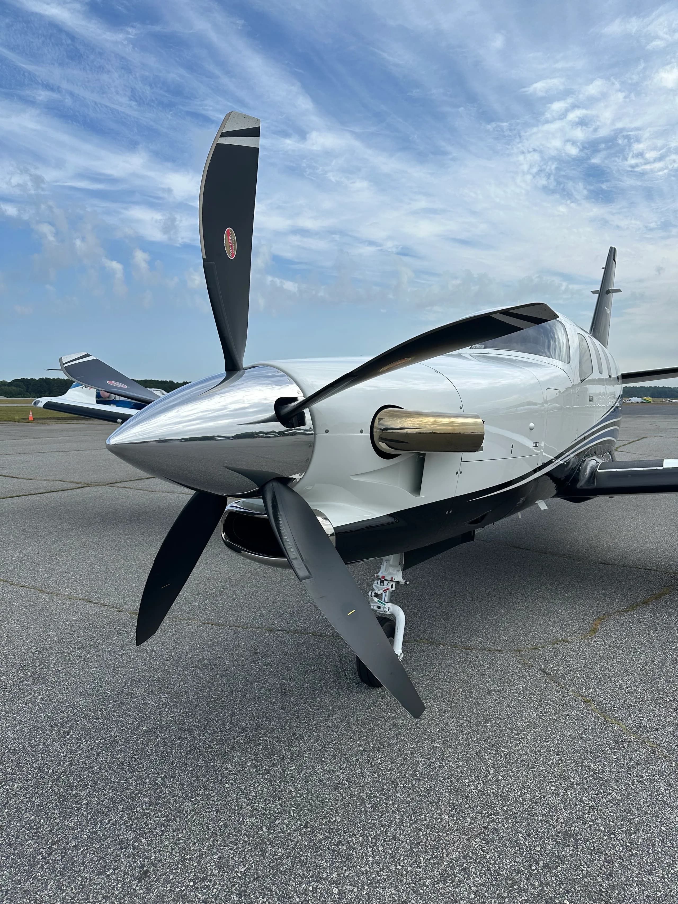 A close-up view of the nose and propeller of a white and blue TBM 960 aircraft on the tarmac.