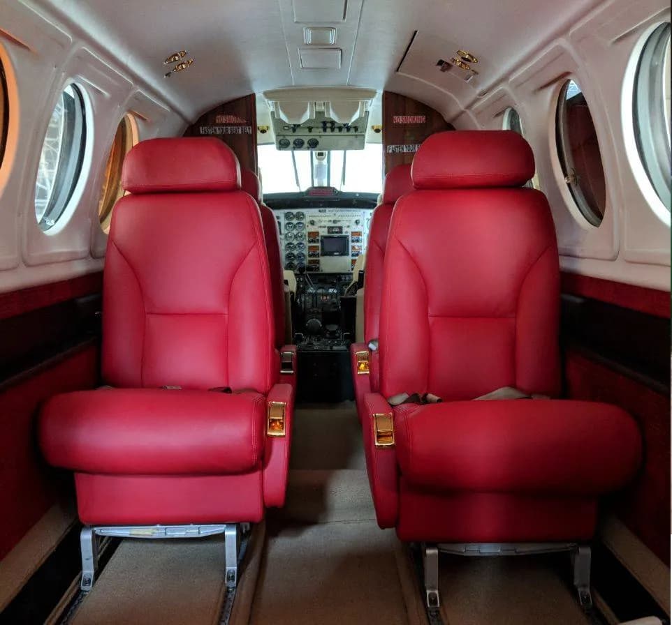 The aircraft cabin interior with two rows of red leather seats facing the cockpit.