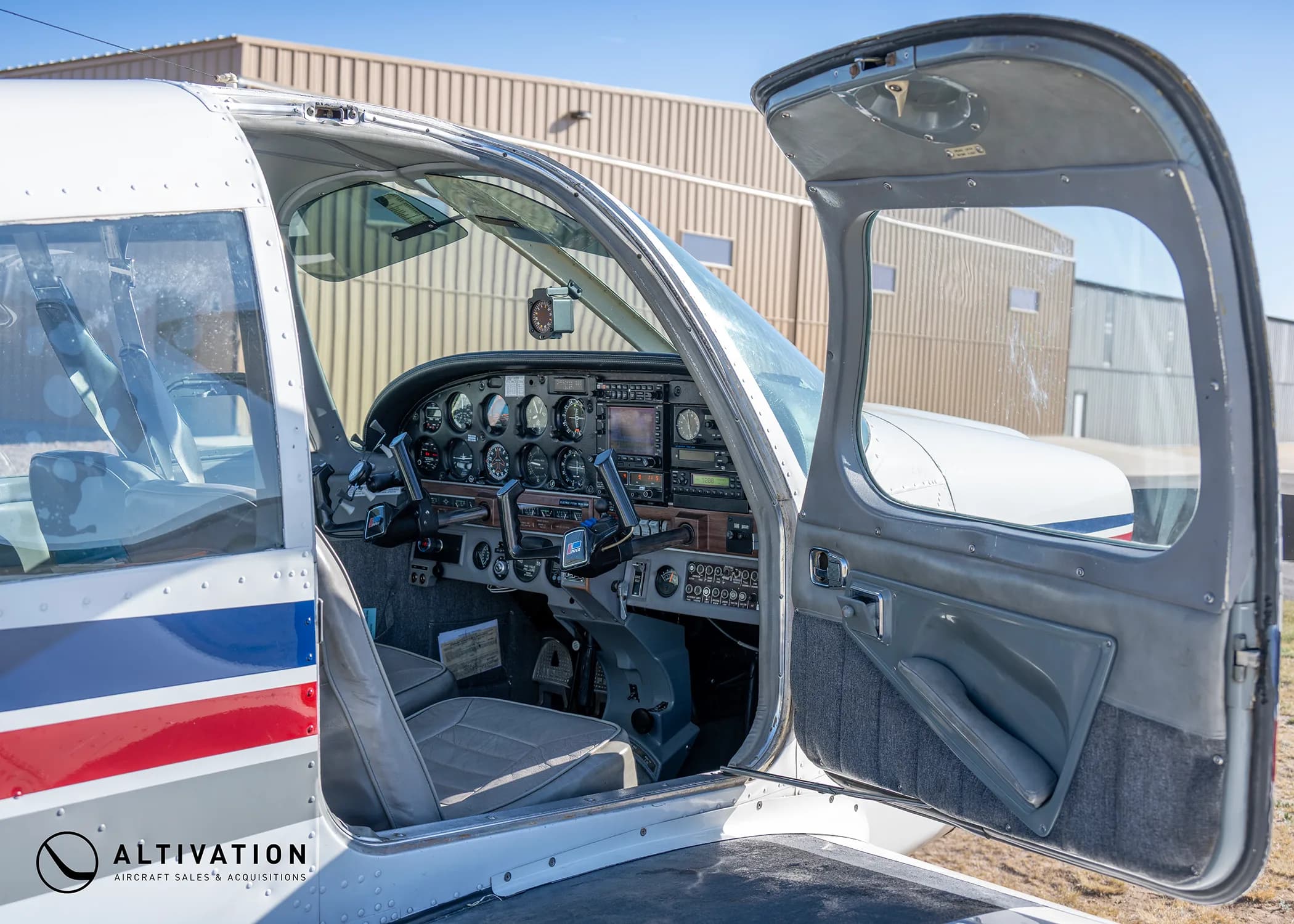 The open door of a Piper Cherokee aircraft, revealing the gray interior and cockpit.