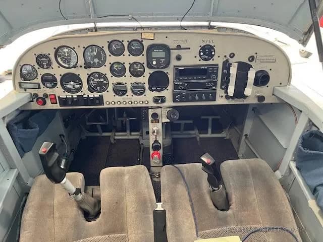A detailed view of the instrument panel and controls in the cockpit of a light aircraft, showing gauges, radios, and joysticks.